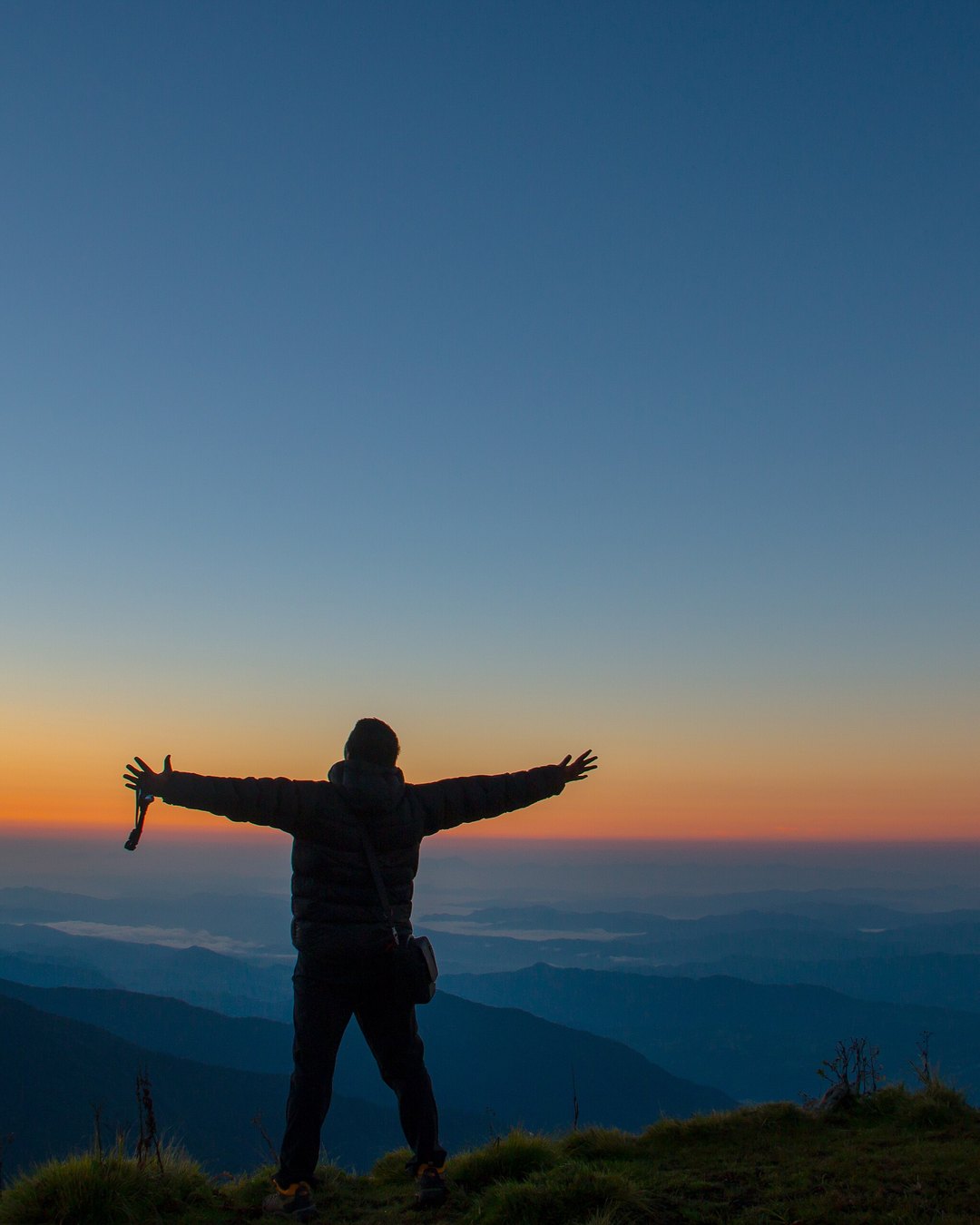 A hiker with arms outstretched watching sunrise from a Himalayan summit